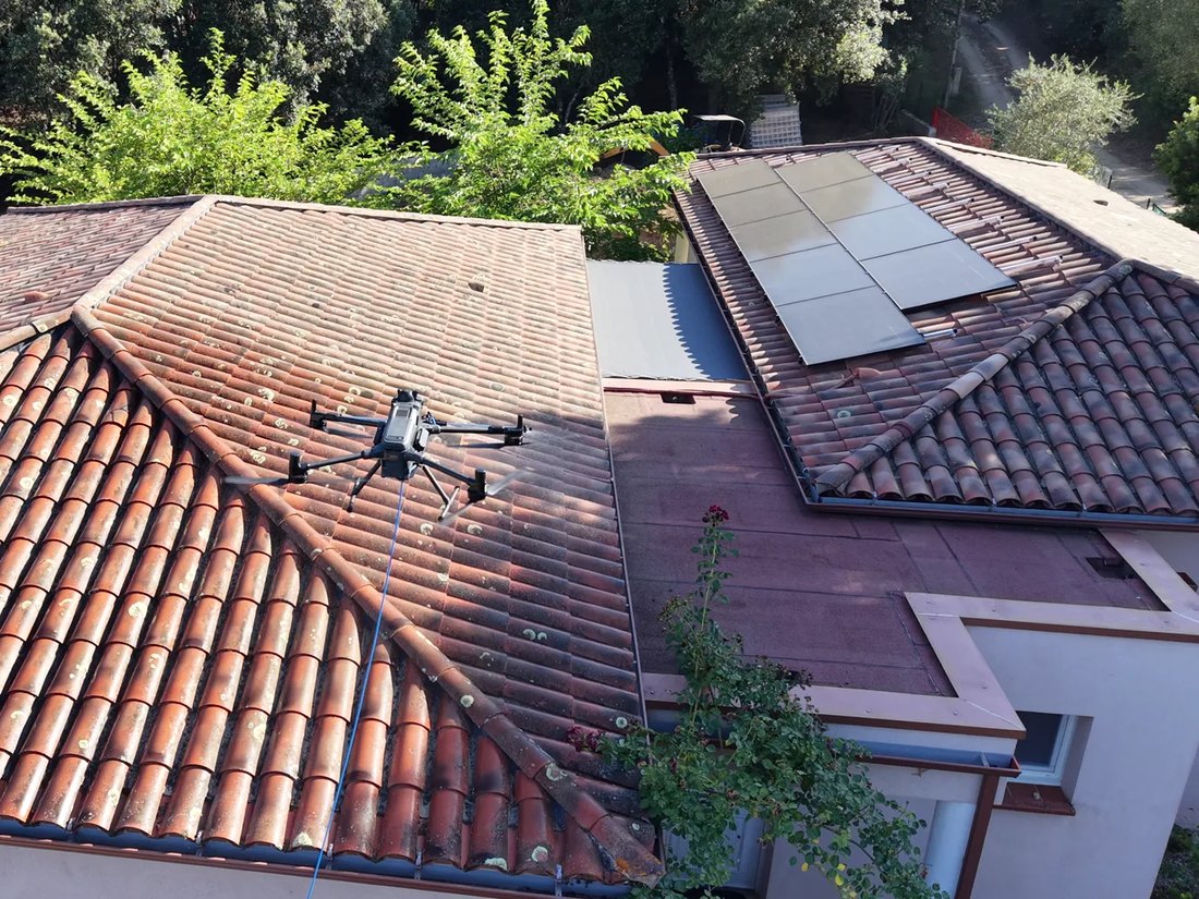 Drone équipé d'un système de pulvérisation en intervention sur une toiture équipée de panneaux photovoltaïques
