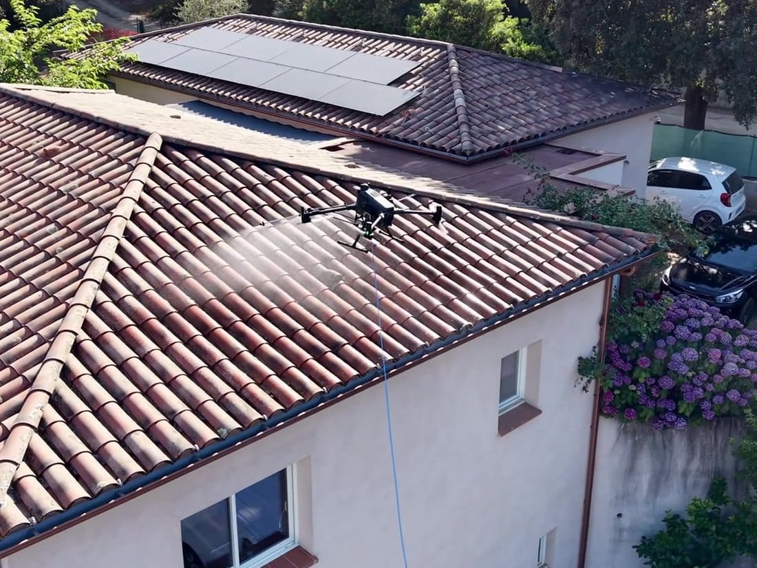 Drone de pulvérisation de Drone Solution Pro Corse traitant une toiture en tuiles, alimenté par son tuyau depuis le sol