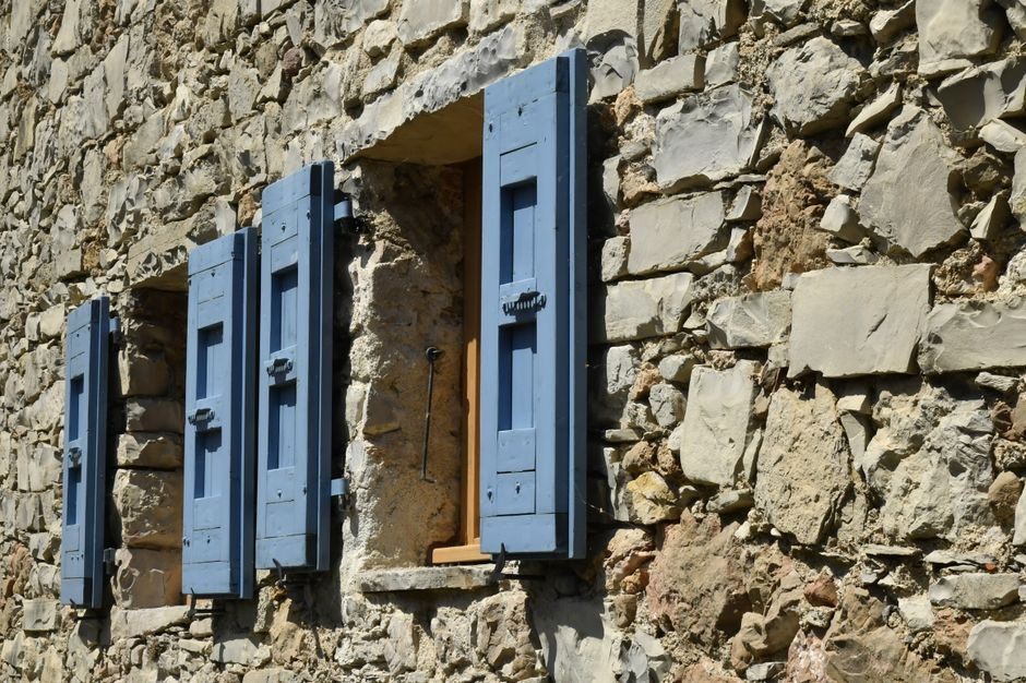 Mur en pierre traditionnelle et volets bleus d'une maison de village